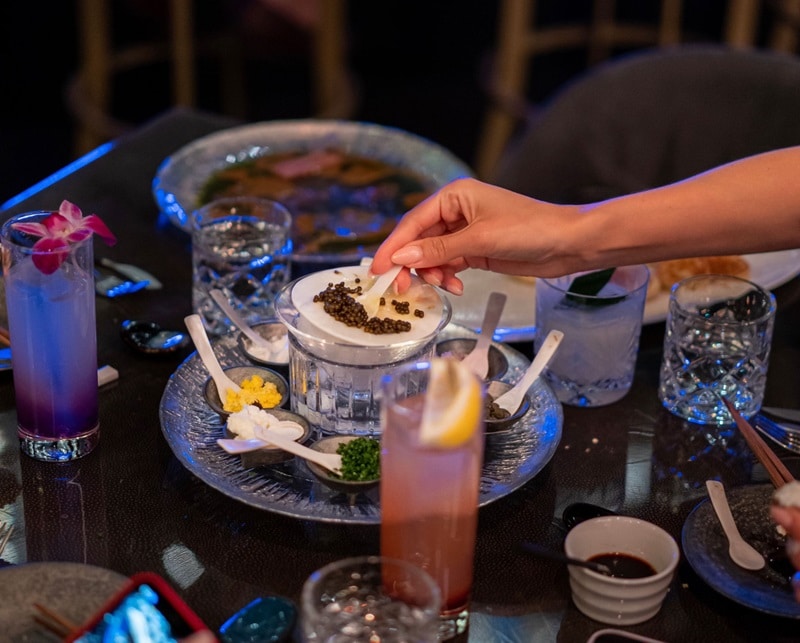 A person reaching for caviar at Aqua Seafood & Caviar.