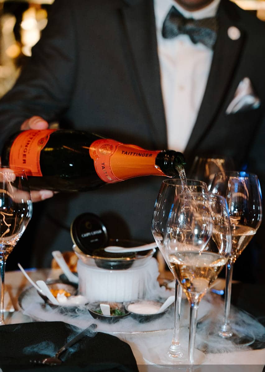A server pouring champagne for guests at Aqua Seafood & Caviar Restaurant.